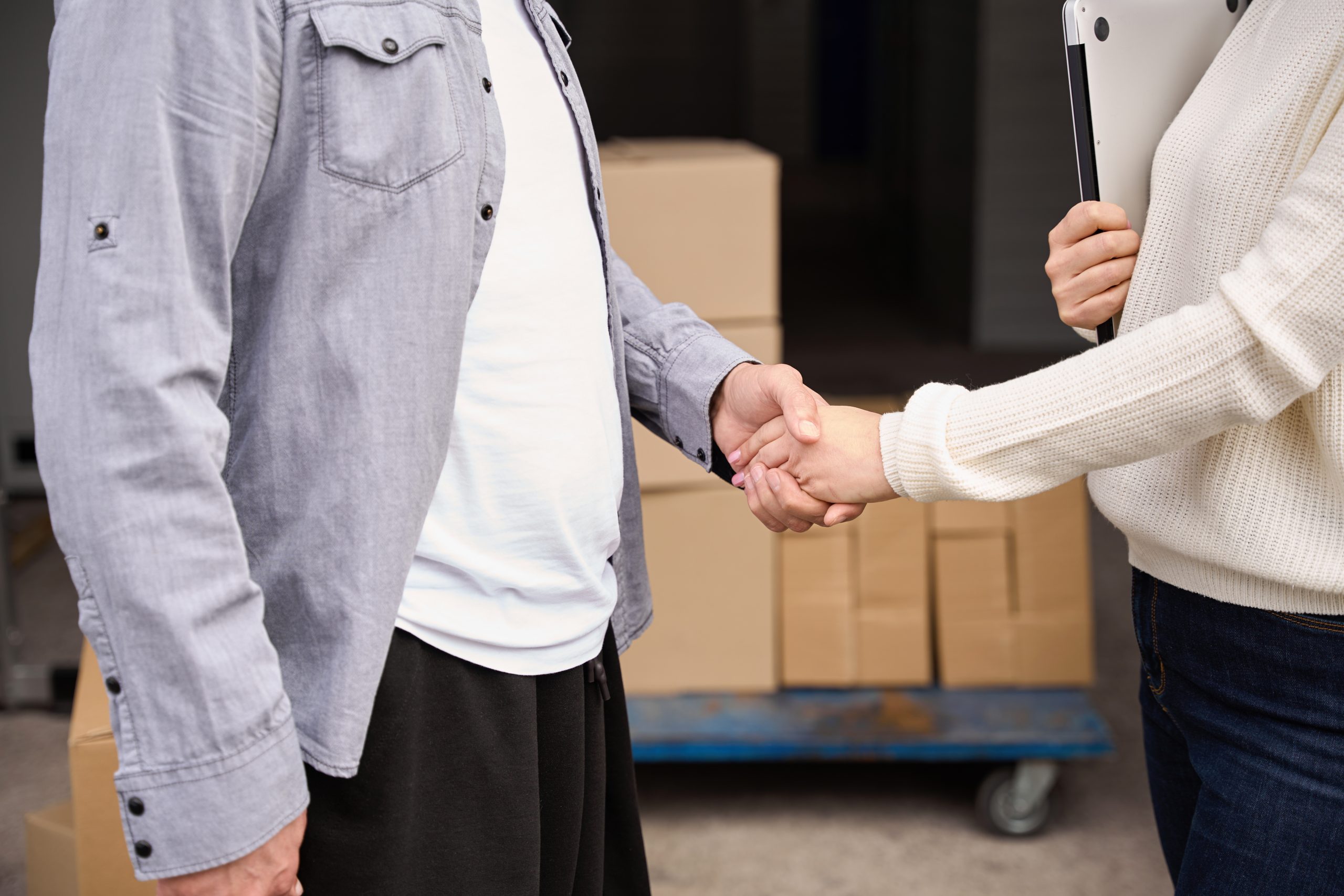 Man holding standing near trolley with stacked boxes near storehouse and shaking hands to female